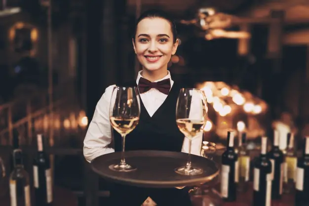 Smiling server holding a tray with two wine glasses in an elegant restaurant setting